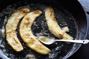 bananas cooking in butter in a cast iron pan with a spoon