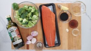 salmon, broccoli, garlic, ginger, soy sauce, salt and pepper, olive oil lay out on a chopping board