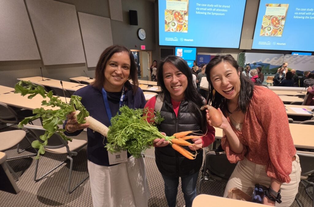3 dietitians holding fresh vegetables, radish, carrot, onion in their hands and smiling at the camera in an auditorium